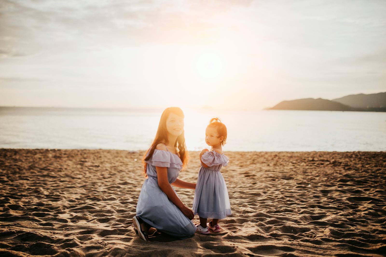 A mother and daughter share a tender moment on the beach at sunset, capturing the essence of love and nature.