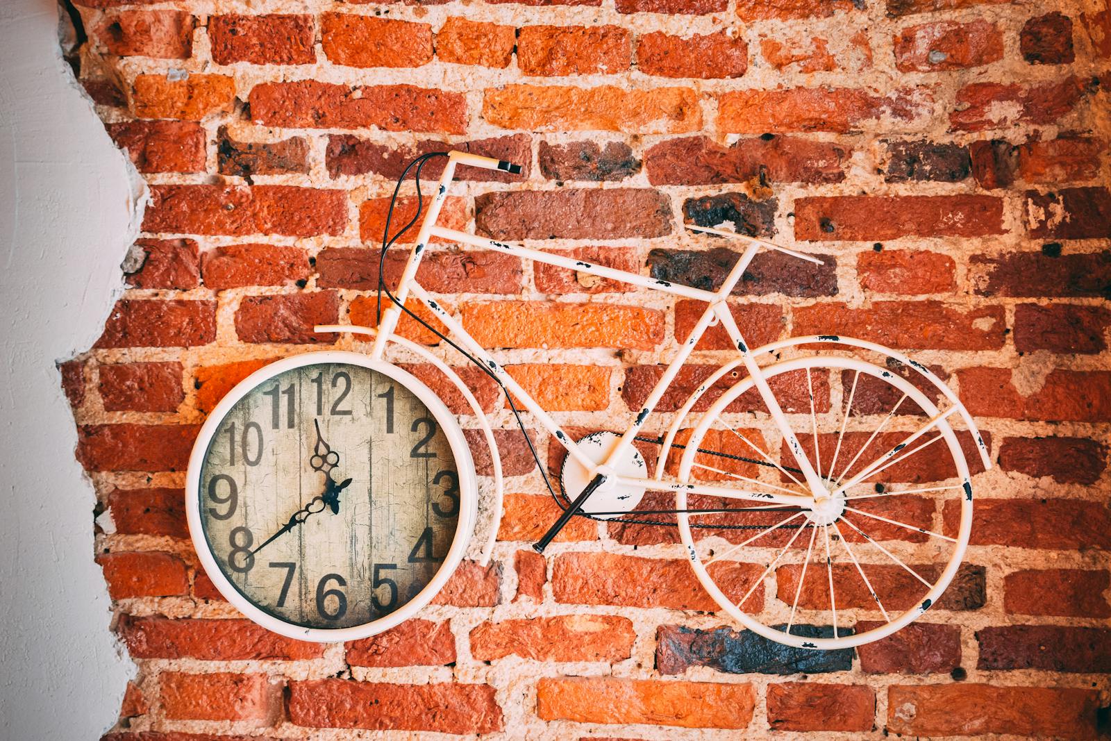 A vintage-style wall clock integrated into a metal bicycle frame on an exposed brick wall.