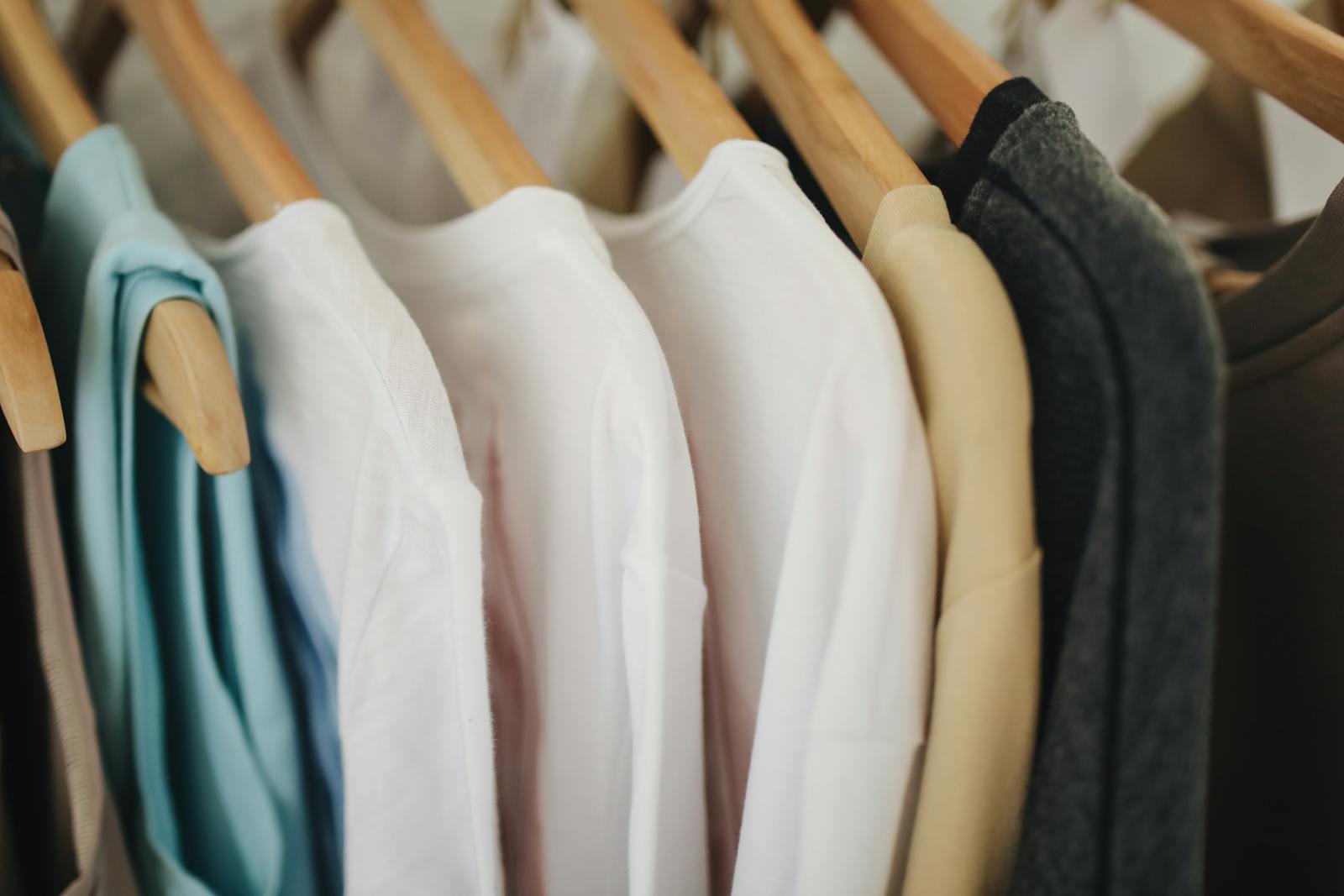 A selection of colorful clothes neatly hanging on wooden hangers in a retail store.