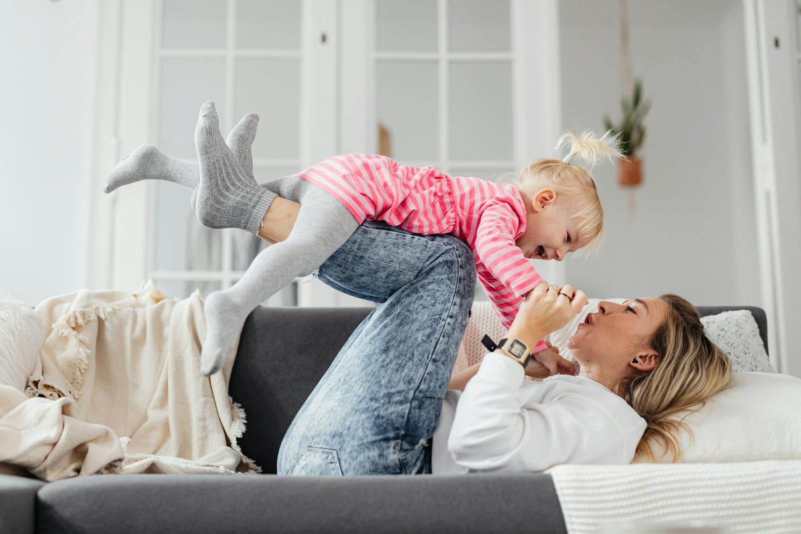 A joyful mother and daughter spend playful moments together on a couch, enhancing their bond.