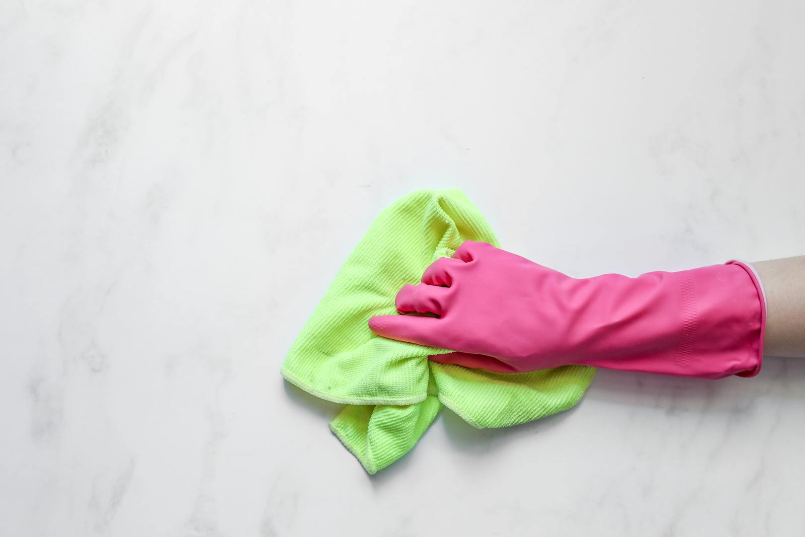 Pink rubber glove cleaning a surface with a green cloth on a white background.